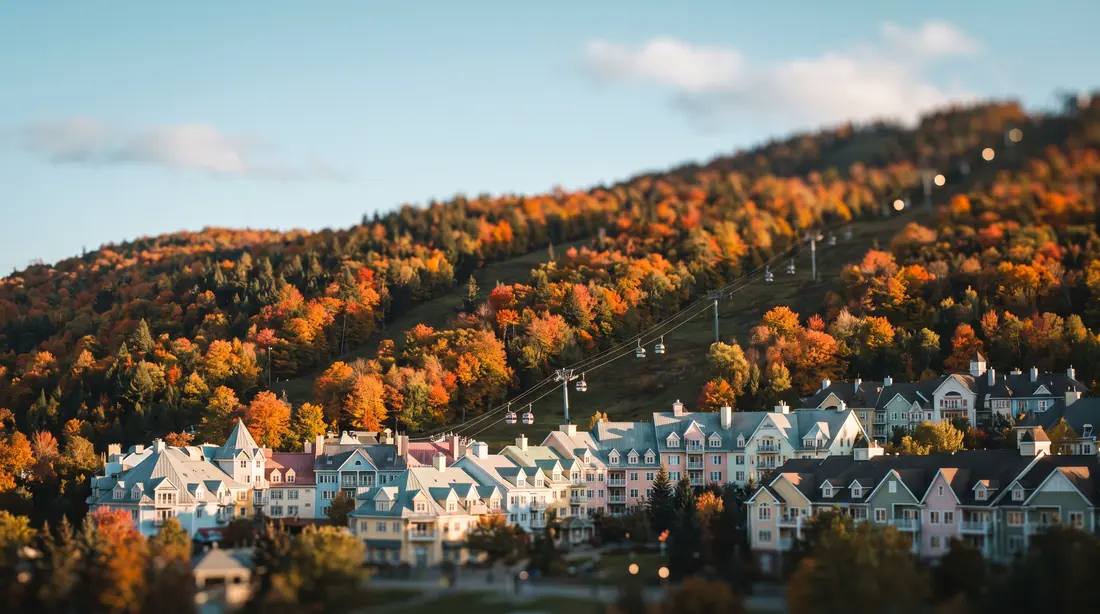 A resort village with pastel facades at the foot of a ski hill in autumn colours, with a gondola line